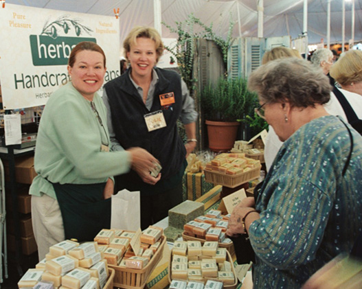 A photo from 2002 of our Founder LaRee Gilberg with her sister selling soap at a market booth