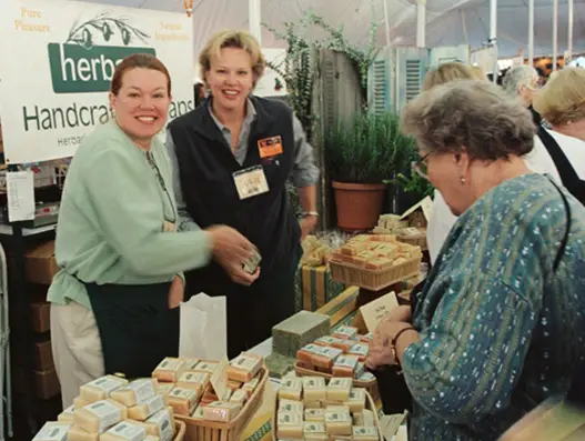 A photo from 2002 of our Founder LaRee Gilberg with her sister selling soap at a market booth