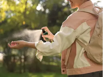 A person outdoors spraying Herbaria natural insect repellent on their arm for DEET-free protection.