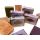 A collection of various handcrafted soap bars in different colors like green, orange, and purple, some in paper wraps and others unwrapped, arranged on a white surface.