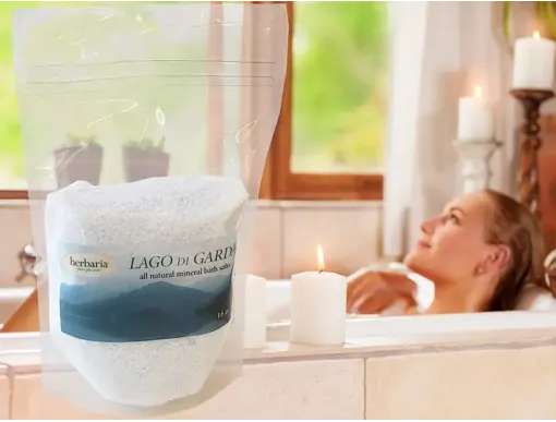 woman bathing in tub with candles and a bigger picture of Herbaria bath salts over top of the image