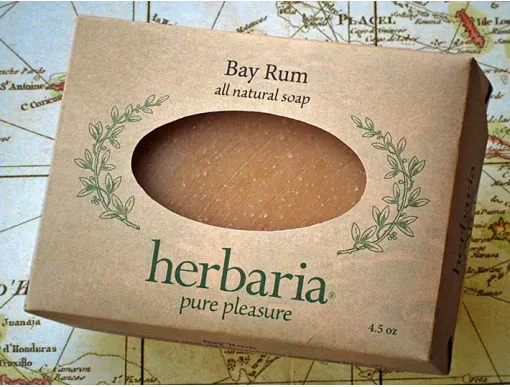 A bar of Herbaria Bay Rum all-natural soap in a kraft paper label with an oval cutout, displayed on a vintage map background
