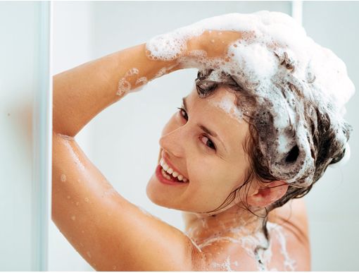A woman joyfully shampooing her hair with Herbaria shampoo bars in the shower.