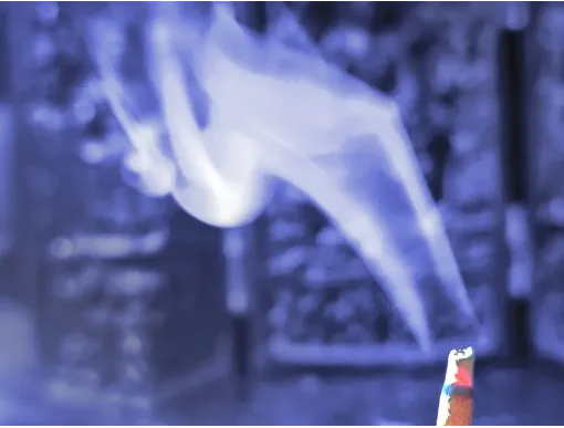 Wisps of blue-toned smoke curling upward from a lit herbal incense stick.