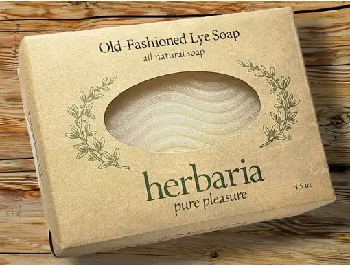 Handmade old-fashioned lye soap bar with wavy pattern wrapped in paper on a wooden surface.