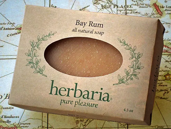A bar of Herbaria Bay Rum all-natural soap in a kraft paper label with an oval cutout, displayed on a vintage map background
