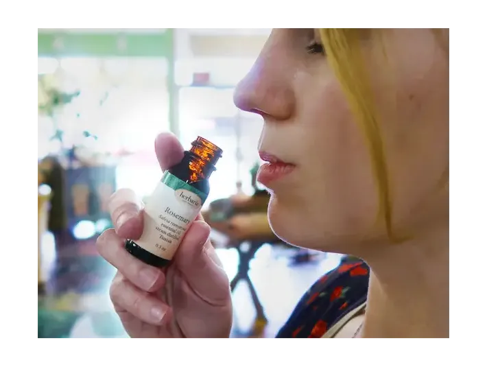 Close-up profile of Herbaria employee Bekka holding a small amber glass bottle up to her nose to smell the essential oil.