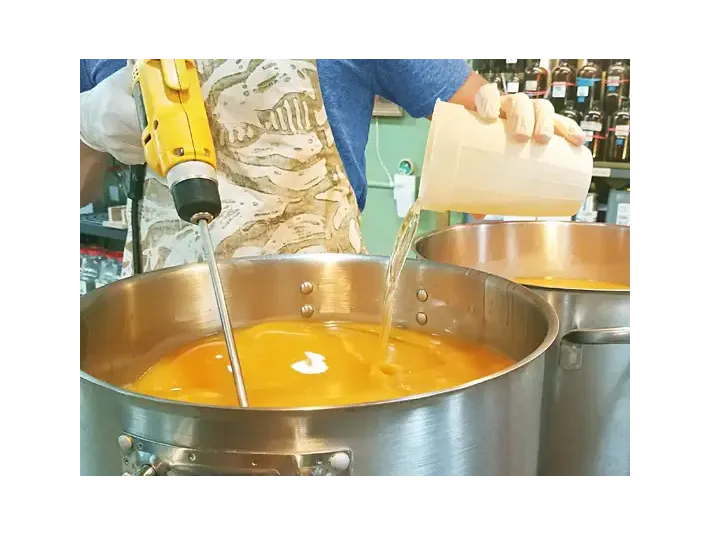 Blake mixing soaps and the added essential oils in a large stainless steel pot with an electric hand-held mixer.