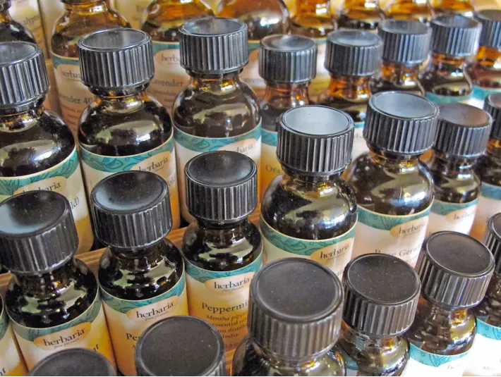 Close-up of rows of small amber glass bottles of essential oils with black ribbed caps and light-colored Herbaria labels.