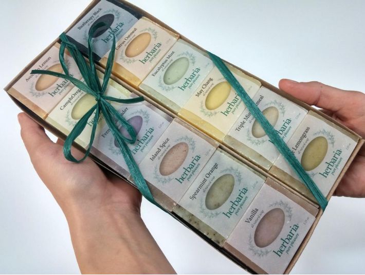 A tray of 12 herbaria half bar soaps being held by two hands.