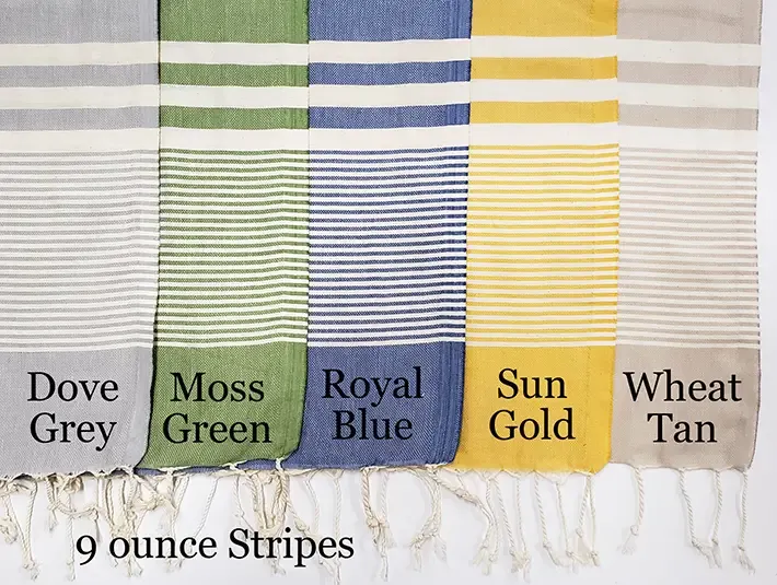 Five 9-ounce striped Turkish towels displayed side-by-side in Dove Grey, Moss Green, Royal Blue, Sun Gold, and Wheat Tan with white horizontal stripes and knotted fringe.