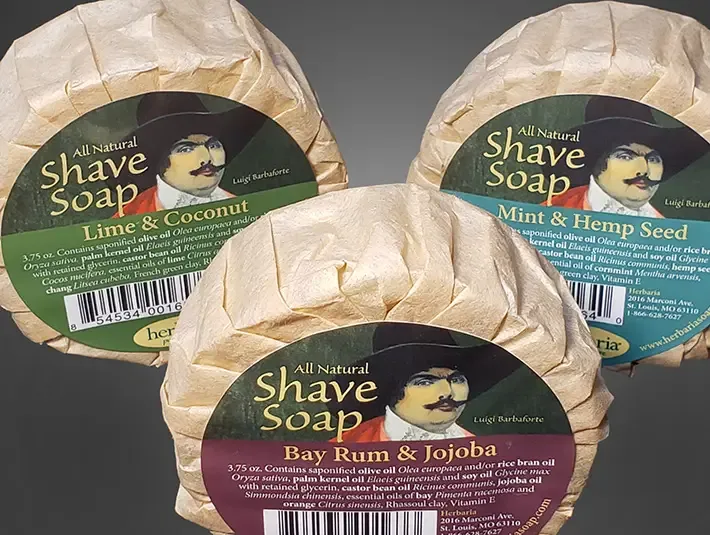 A set of 3 round bars of Herbaria all-natural shave soap featuring the embossed Herbaria logo on a rustic brown paper wrap.